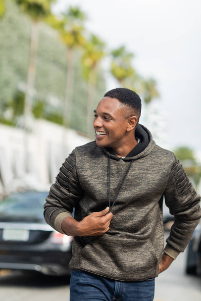 happy african american man in hoodie and jeans walking on street in Miami  - Фото, зображення