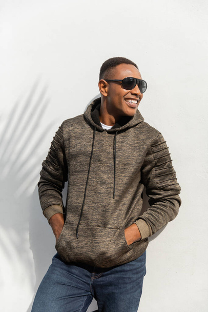 happy african american man in sunglasses standing with hands in pockets near white wall  - Foto, Imagem