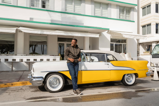 MIAMI, FLORIDA, EUA - DEZEMBRO 15, 2022: homem afro-americano alegre de pé perto do clássico carro retro  - Foto, Imagem