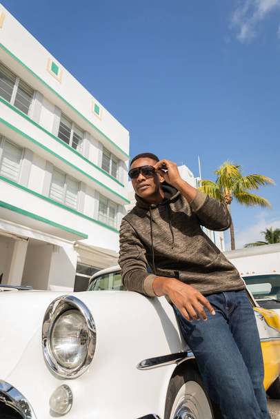 MIAMI, FLORIDA, Estados Unidos - 15 DE DICIEMBRE DE 2022: hombre afroamericano con gafas de sol cerca de un auto de época  - Foto, imagen