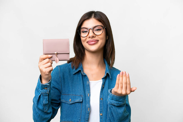 Young Russian woman holding a wallet over isolated white background inviting to come with hand. Happy that you came - 写真・画像
