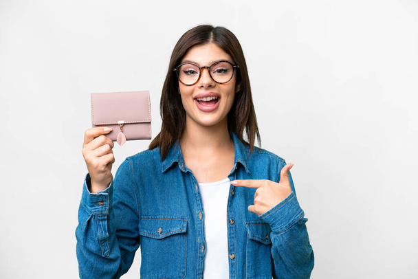 Молода російська жінка тримає гаманець над ізольованим білим фоном з несподіваним виразом обличчя. - Фото, зображення