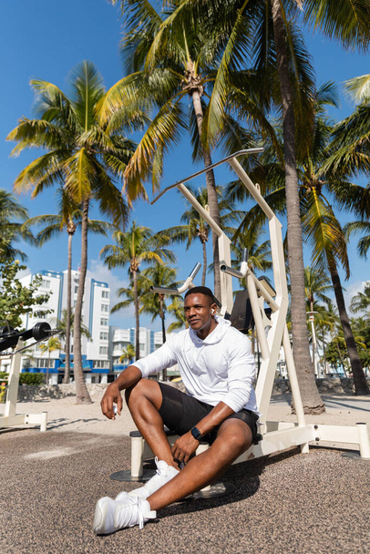 african american sportsman in wireless earphone resting after workout in Miami beach  - 写真・画像