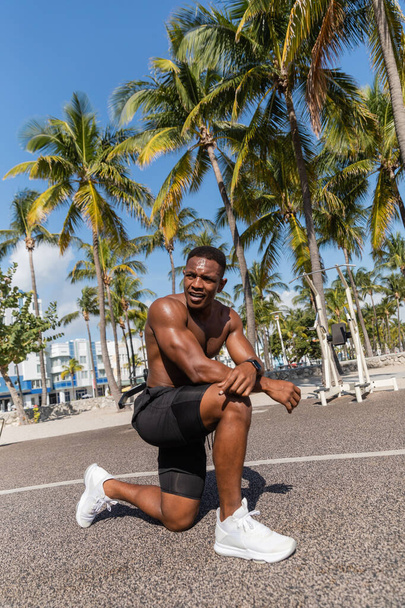 マイアミのヤシの木の隣のトレーニングの後に休むシャツレスのアフリカのスポーツマン - 写真・画像
