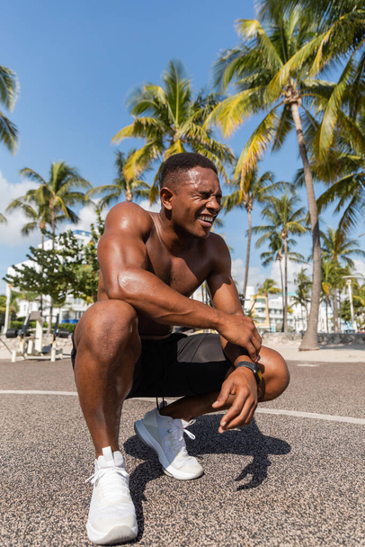 happy african american sportsman in shorts and sneakers smiling after workout next to palm trees in Miami - Φωτογραφία, εικόνα