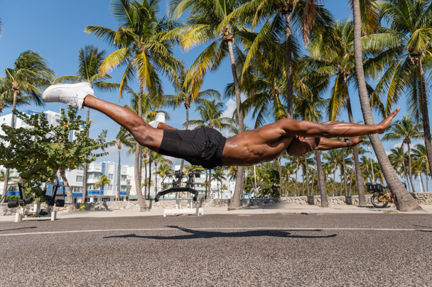 マイアミビーチの緑のヤシの木の隣に浮かぶシャツレスのアフリカ系アメリカ人のスポーツマン  - 写真・画像