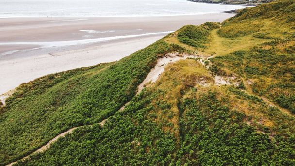 Egy magas domb lejtője a homokos tengerparton. Zöld fű borította hegy mellett tenger - Fotó, kép