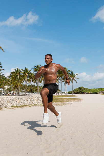 athletic african american man in shorts and sneakers running on sand next to palm trees in Miami beach - Foto, Imagem