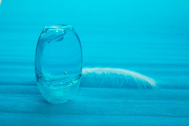 Gel antisettico tascabile in un contenitore blu su fondo blu. Bolle d'aria nel gel. Piuma bianca accanto all'antisettico - Foto, immagini