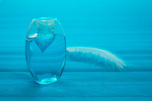 Gel antiséptico de bolsillo en un recipiente azul sobre un fondo azul. Burbujas de aire en el gel. Pluma blanca junto al antiséptico - Foto, imagen