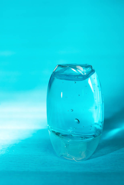 Gel disinfettante per mani antisettico tascabile isolato su sfondo blu, senza etichetta. Piccola bottiglia di liquido antibatterico blu trasparente con bolle di ossigeno, granuli rotondi. Alcole idroalcolico, etilico.  - Foto, immagini