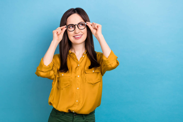 Photo of dreamy charming lady dressed yellow shirt arms eyewear looking empty space isolated blue color background. - Zdjęcie, obraz