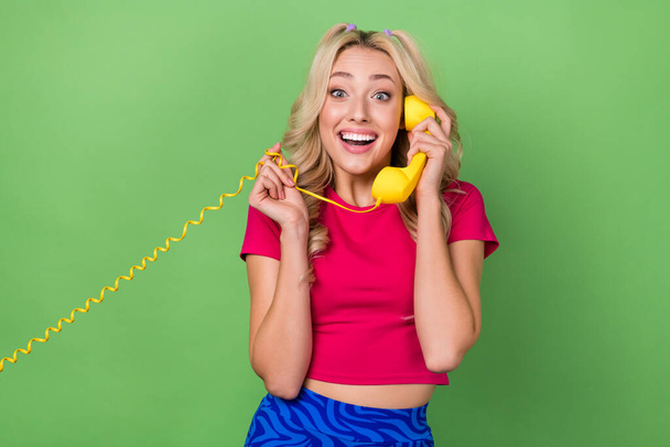 Foto di eccitato positivo ridere ragazzina giovane signora positiva tenere cavo giallo vintage telefono chiamando amico isolato su sfondo di colore verde. - Foto, immagini