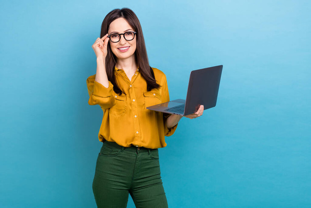 Photo of smile young lady brunette hair wear yellow shirt green pants fix specs hold computer boss working office isolated on blue color background. - Fotografie, Obrázek