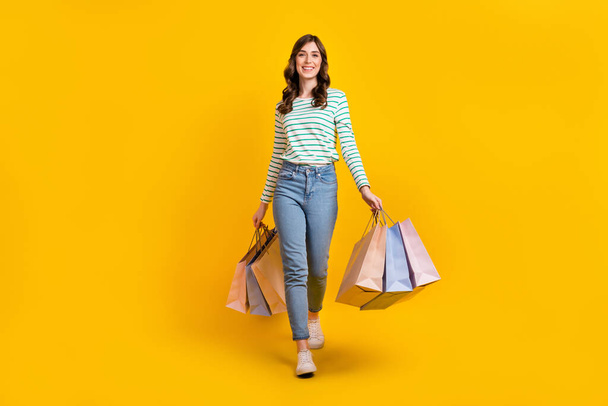Full size photo of gorgeous woman with curly hairstyle striped denim pants hold bags go shopping isolated on yellow color background. - Fotografie, Obrázek