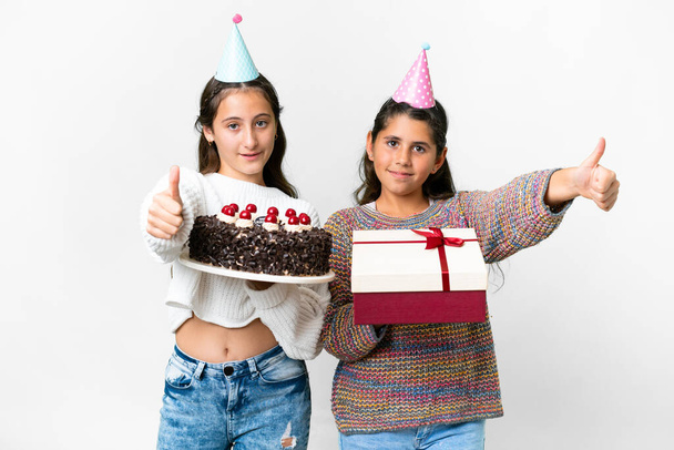 Друзі дівчата тримають подарунок і торт на день народження над ізольованим білим тлом, даючи великі пальці вгору жестом, тому що сталося щось хороше
 - Фото, зображення