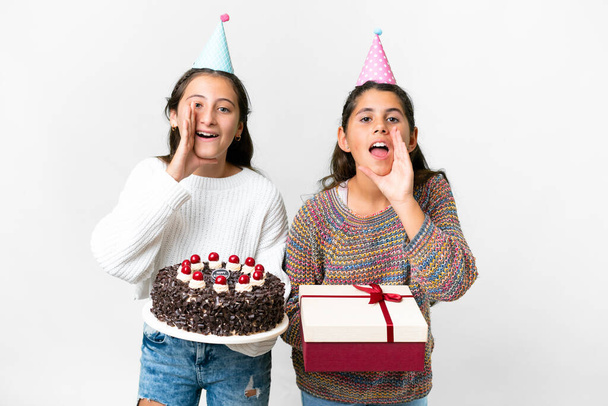Amigos niñas sosteniendo regalo y un pastel de cumpleaños sobre fondo blanco aislado gritando y anunciando algo - Foto, imagen