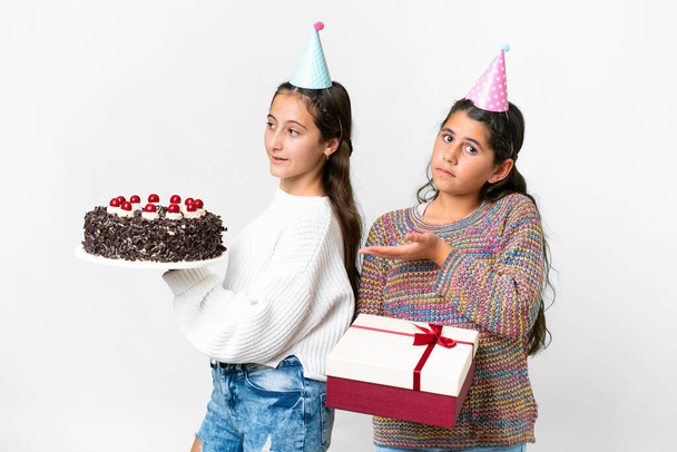 Amigos niñas sosteniendo regalo y un pastel de cumpleaños sobre fondo blanco aislado extendiendo las manos a un lado para invitar a venir - Foto, imagen