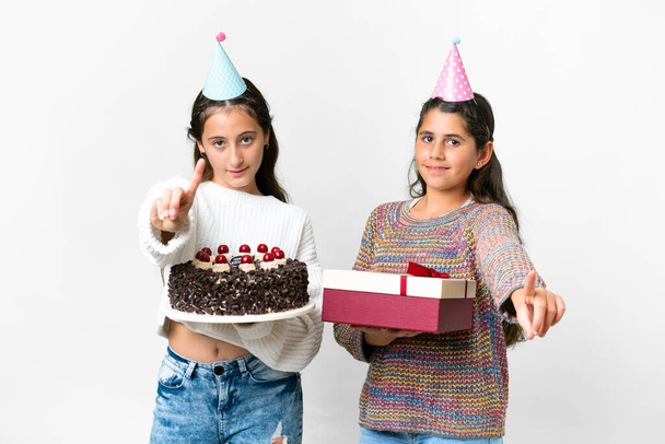 Друзі дівчата тримають подарунок і торт на день народження над ізольованим білим тлом, показуючи і піднімаючи палець
 - Фото, зображення