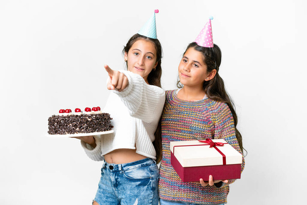 Přátelé dívky drží dárek a narozeninový dort přes izolované bílé pozadí ukazuje na stranu prezentovat produkt - Fotografie, Obrázek