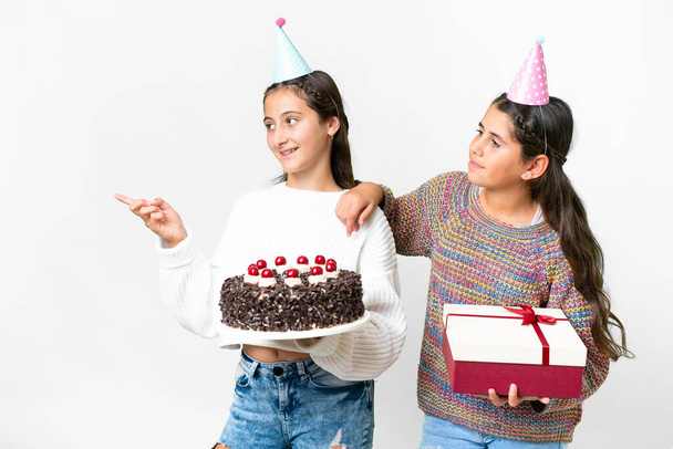 Friends girls holding gift and a birthday cake over isolated white background presenting an idea while looking smiling towards - Photo, Image