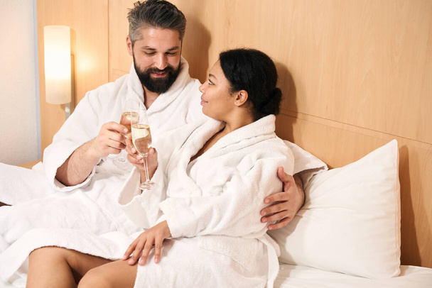 Happy young male and his female companion clinking glasses of champagne in bed - Foto, Bild
