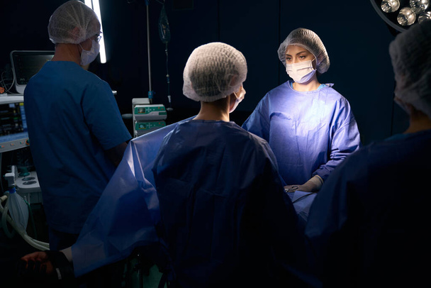 Grupo de pessoas em macacão cirúrgico ficar na mesa de operação, pessoas em máscaras protetoras - Foto, Imagem