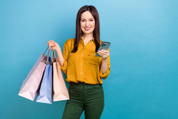 Photo of cheerful positive lady dressed yellow shirt holding bargains chatting device empty space isolated blue color background. - Фото, зображення