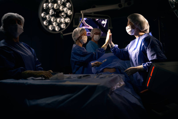 Cirujano y el asistente dan cinco altos después de una operación exitosa, el paciente se acuesta en la mesa de operaciones - Foto, imagen