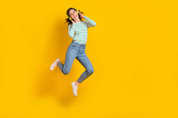 Full size photo of good mood gorgeous woman dressed striped shirt jeans shoes arms touching headphones isolated on yellow color background. - Valokuva, kuva