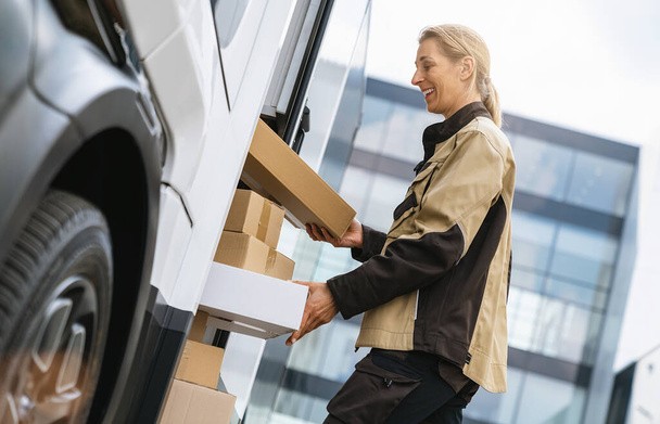 Kobieta odbierająca paczki z furgonetki, żeby dostarczyć je klientowi. Wizerunek koncepcji dostawy kuriera - Zdjęcie, obraz