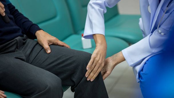 Doctor physiotherapist examining treating injured knee of senior patient at hospital. Doctor examining him patient knee in Hospital. Doctor checking patient with knee to determine the cause of illness - Φωτογραφία, εικόνα