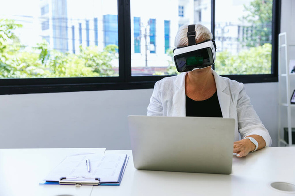Business Woman in VR headset. Woman using VR glasses for online game. Business woman sitting inside office building with security interface and using virtual reality headset - Photo, image
