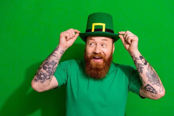 Photo of impressed cool man wear t-shirt arms headwear enjoying shamrock day looking empty space isolated green color background. - Fotografie, Obrázek