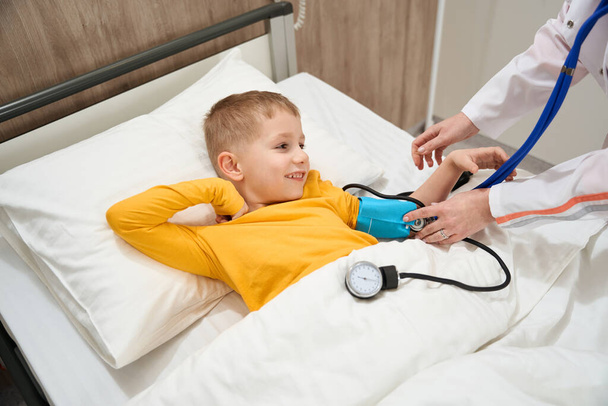 Close-up portret van gelukkig keurig kind op het medisch bed tijdens het onderzoek van de bloeddruk in de kliniek - Foto, afbeelding