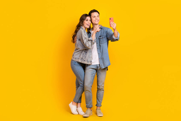 Full length photo of attractive sweet couple wear jeans recording video vlog modern device isolated yellow color background. - Foto, Bild