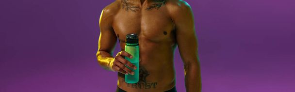 Αθλητικός άνθρωπος με μυώδη γυμνό κορμό κρατώντας μπουκάλι με νερό στο στούντιο φόντο με φίλτρο χρώματος - Φωτογραφία, εικόνα