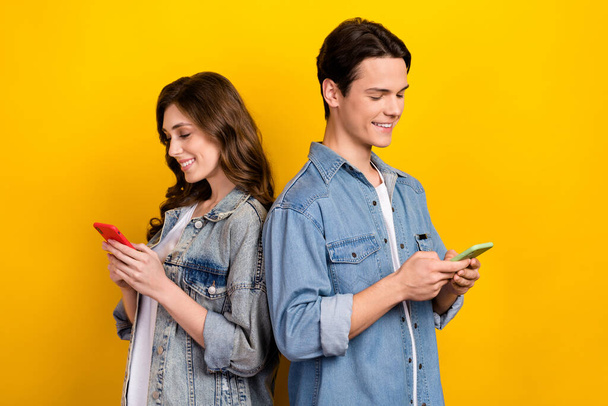 Photo of two cheerful satisfied people use telephone write typing blog post isolated on yellow color background. - Photo, Image