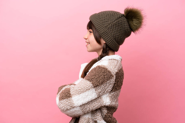 Piccola ragazza caucasica con giacca invernale isolata su sfondo rosa in posizione laterale - Foto, immagini