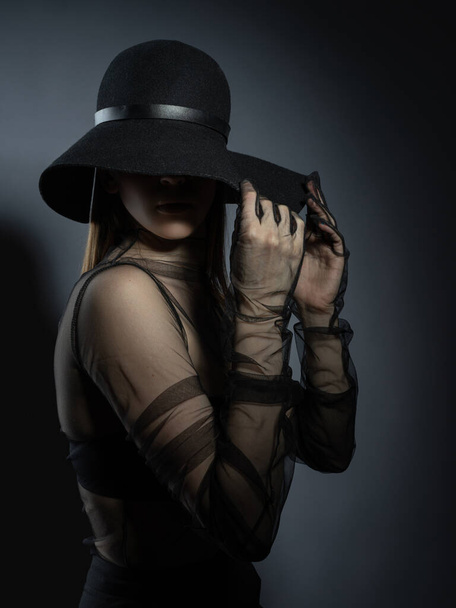 Fashion portrait of a young girl in a black bra and transparent top. Felt black hat. Model posing, faces not visible photo in studio. - Fotoğraf, Görsel