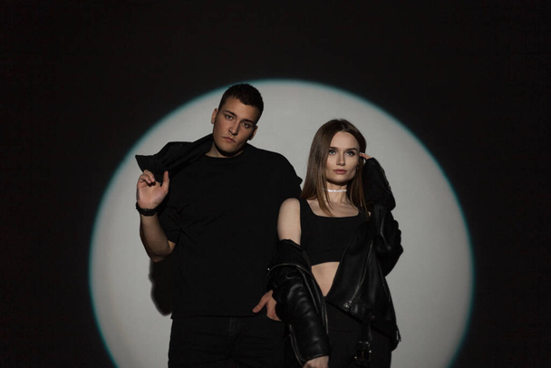 Stylový krásný mladý pár v módní černé ležérní černé oblečení na černém pozadí s kruhovým světlem ve studiu. Hezký muž a krásná dívka na večírku - Fotografie, Obrázek