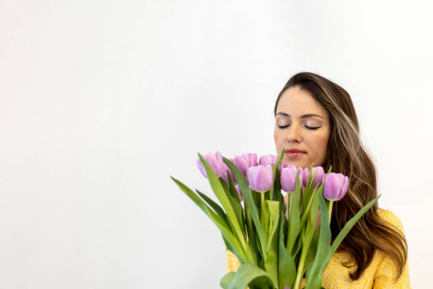 Beautiful happy woman with long hair with a bouquet of tulips in her hands on a white background. Sniffing the flowers. Copy space for text. - Фото, изображение