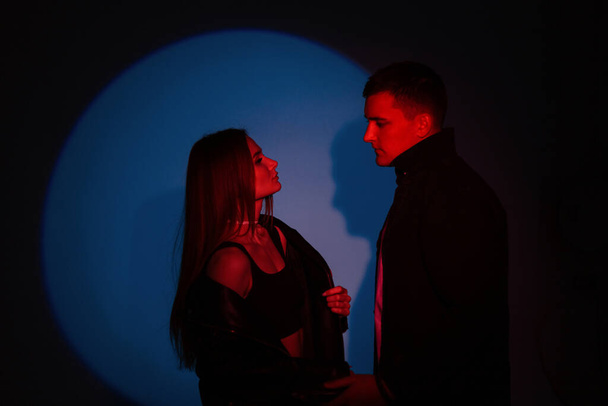 Stylish handsome man and fashionable beautiful girl in fashion clothes on dark background with creative colored red blue light - Fotoğraf, Görsel