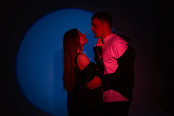 Κομψό όμορφο νεαρό ζευγάρι άντρας και όμορφη γυναίκα σε μοντέρνα ρούχα με κόκκινο φως σε σκούρο μπλε φόντο στο στούντιο - Φωτογραφία, εικόνα