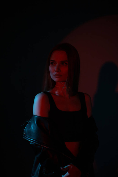Elegante modelo de mujer hermosa sobre fondo oscuro con luz roja - Foto, Imagen