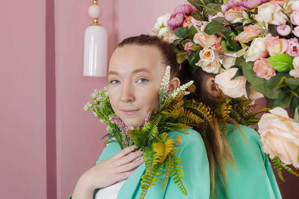 Een mooi meisje in een business pak van malachiet kleur poseren met een plant of bloemen tegen een creatieve roze achtergrond. - Foto, afbeelding