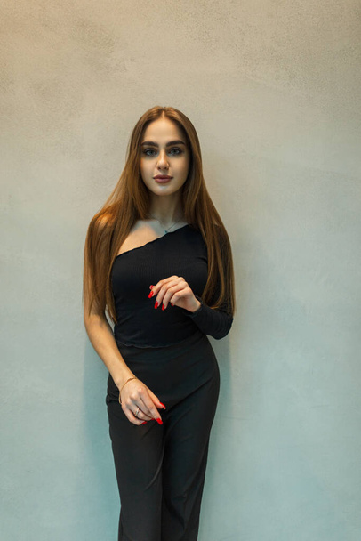 Stylish beautiful business lady in a fashion black clothes with pants and a top near the gray wall - Foto, afbeelding