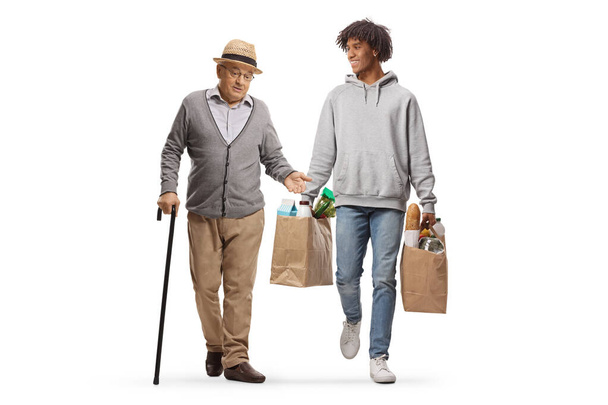 Full length portrait of an african american young man walking with a mature gentleman and carrying grocery bags isolated on white background - Foto, immagini