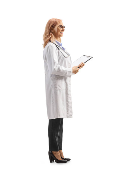 Full length profile shot of a female physician holding a document with a clipboard isolated on white background - Fotó, kép