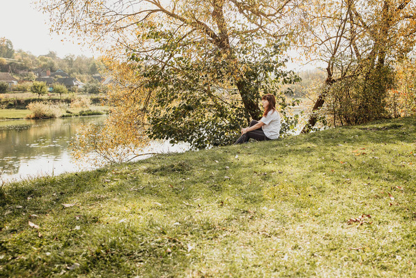 la chica está sentada en la orilla del estanque, el sol brilla, el otoño - Foto, imagen